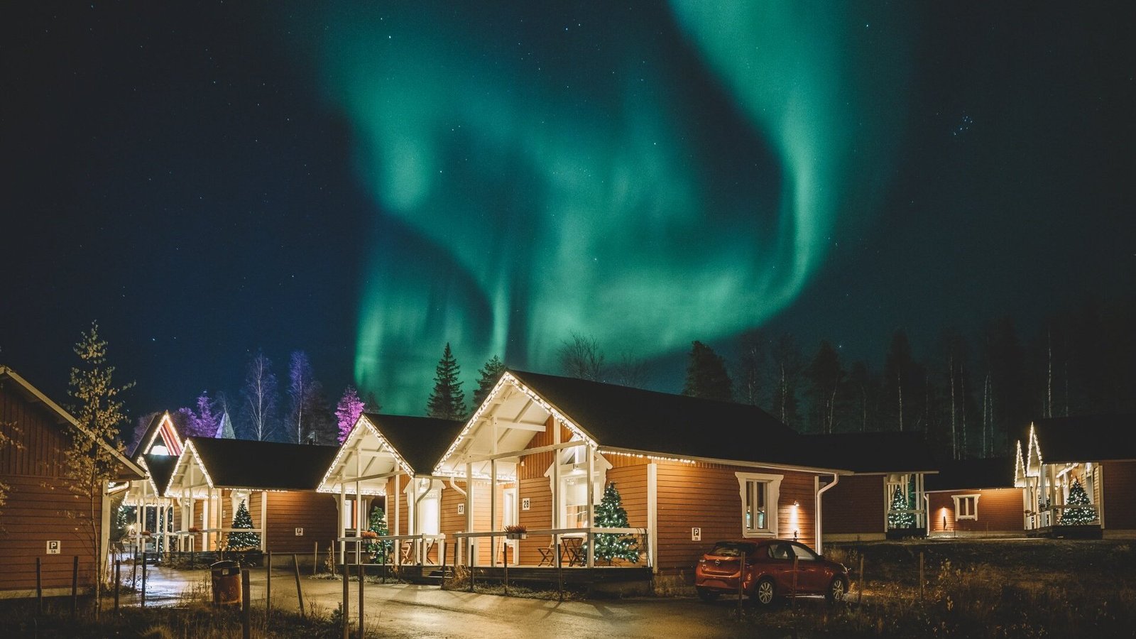 The northern lights over the lit cottages of Santa Claus Holiday Village, Rovaniemi