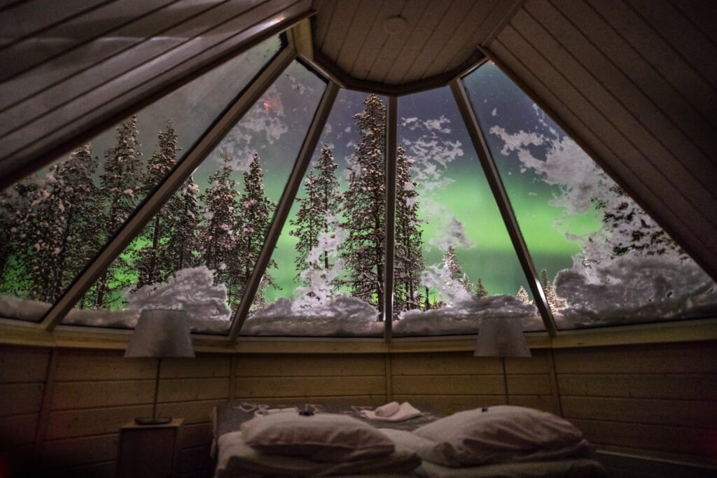 Aurora borealis seen through the glass roof above the bed, Aurora Cabin, Northern Lights Village Saariselkä