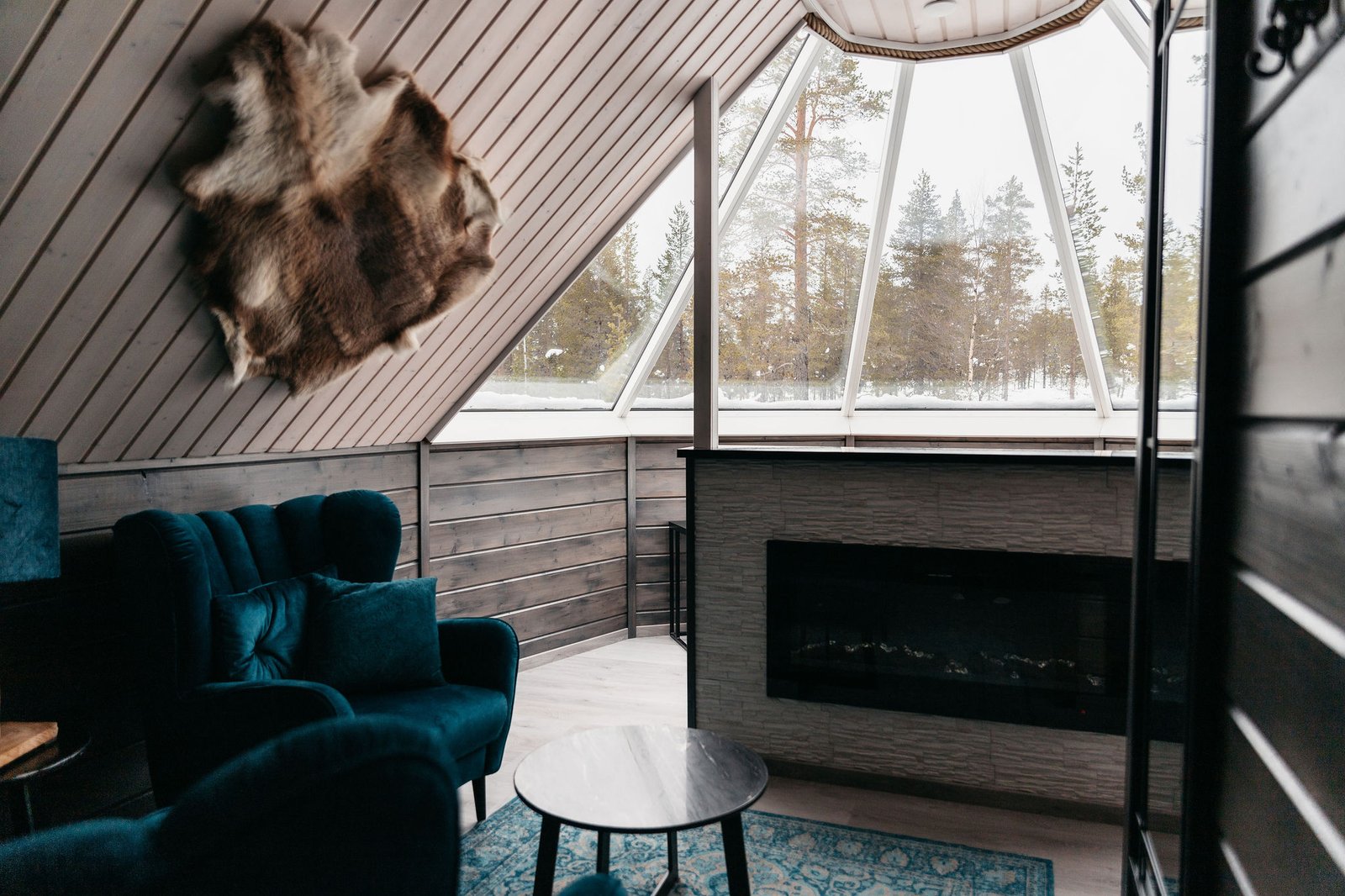 Aurora Cabin living area with fireplace beneath the glass roof, Northern Lights Village Saariselkä