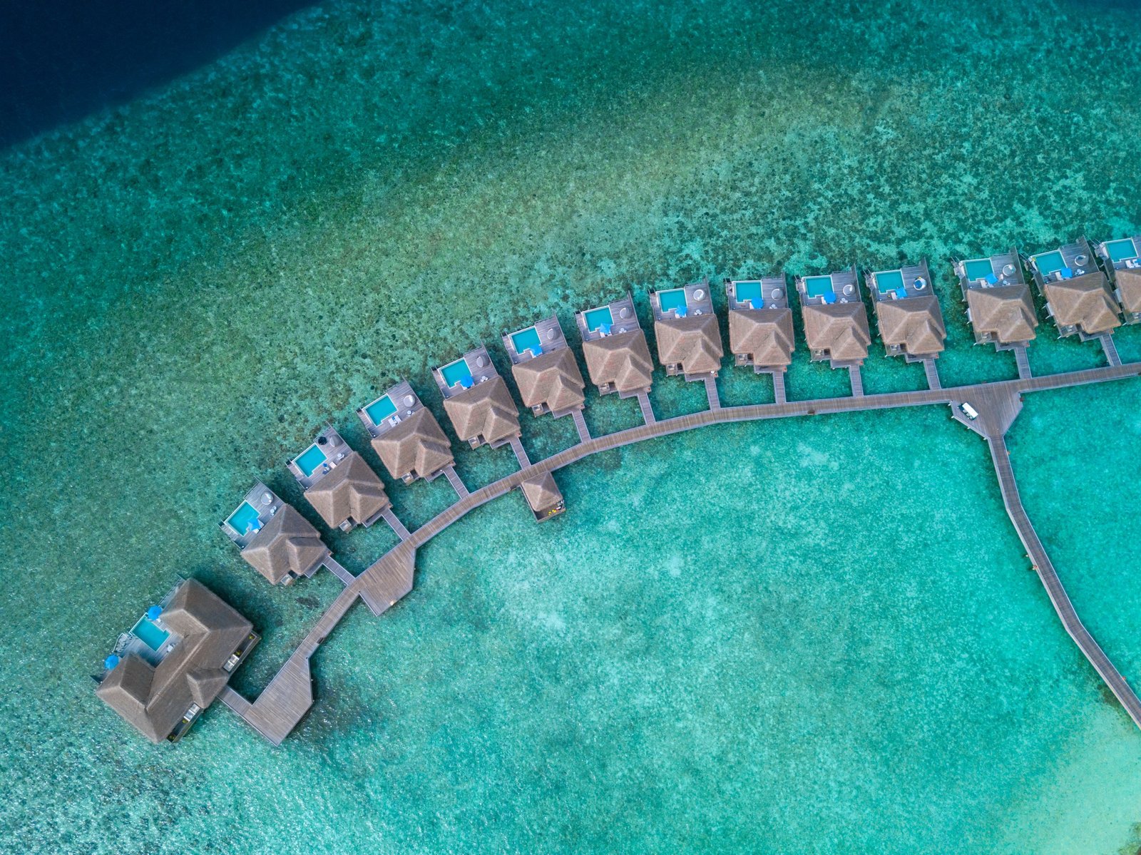 The arc of overwater pool villas over the lagoon at Dusit Thani Maldives, Baa Atoll