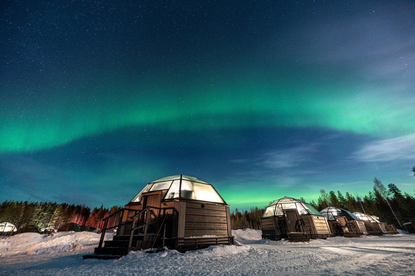 Glass igloos lit from within beneath the northern lights, Arctic SnowHotel, Sinett&auml;