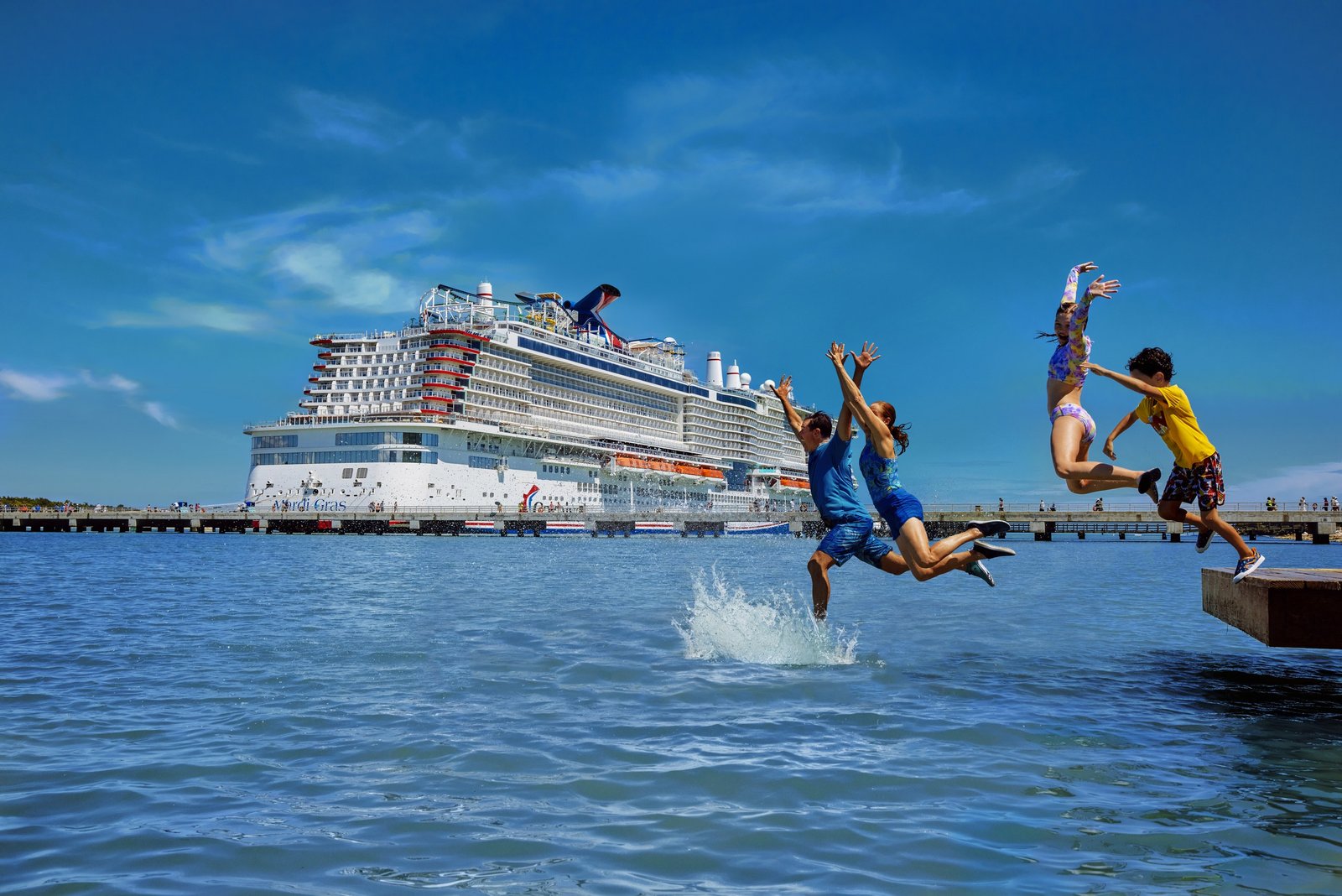 Guests jumping into the water from a pier with a Carnival ship behind