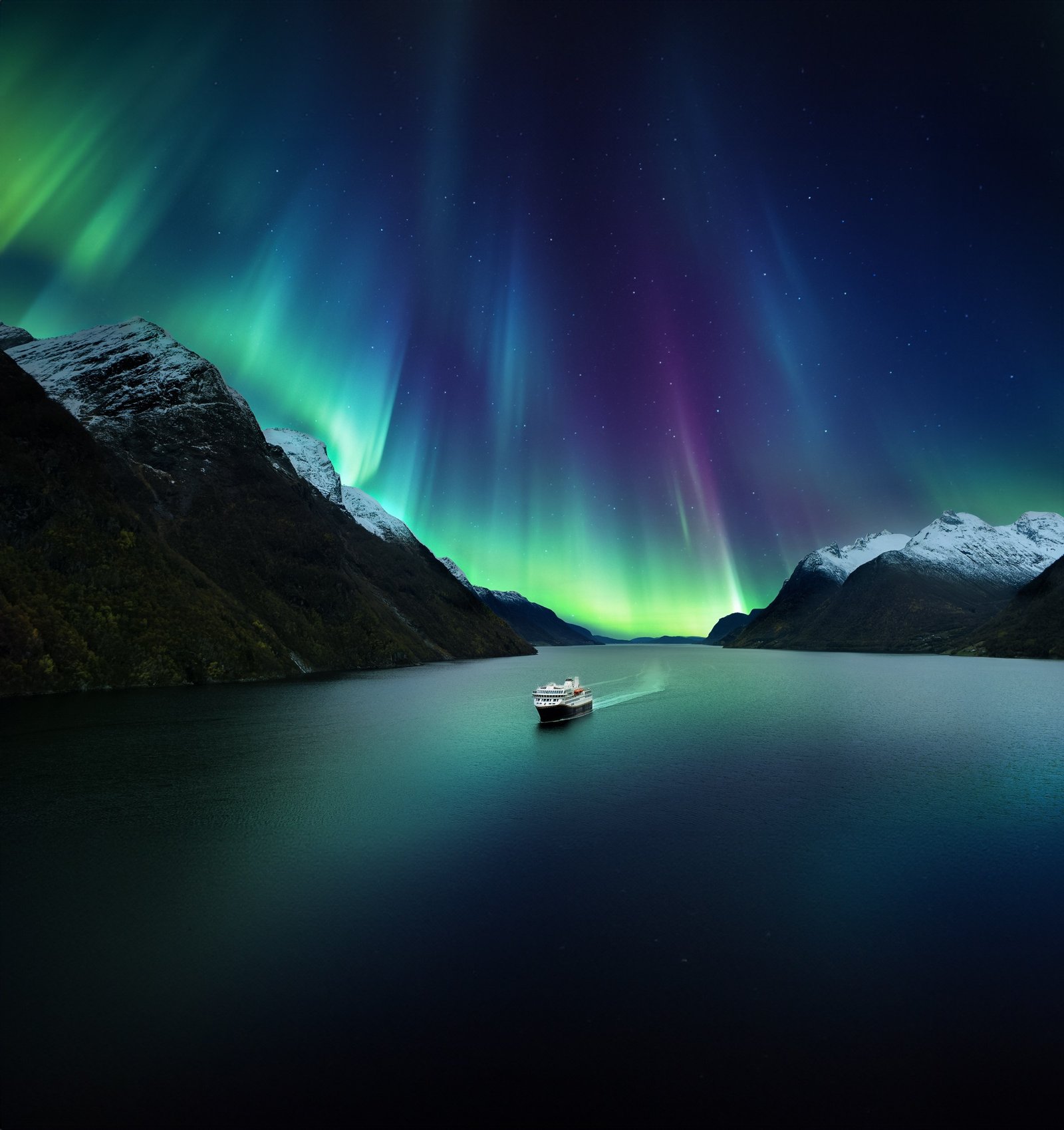 A Havila Voyages ship under the Northern Lights in a Norwegian fjord
