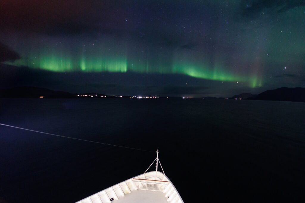 Aurora above the coast, the ship's bow lit below
