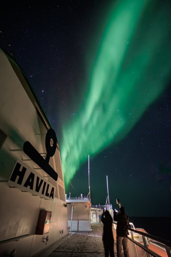 Guests on deck beneath the aurora on the Norwegian coast