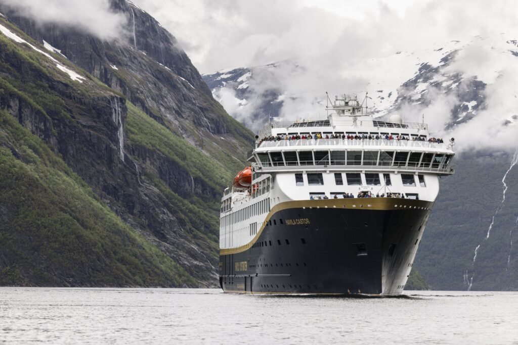 Havila Castor in a Norwegian fjord beneath a waterfall