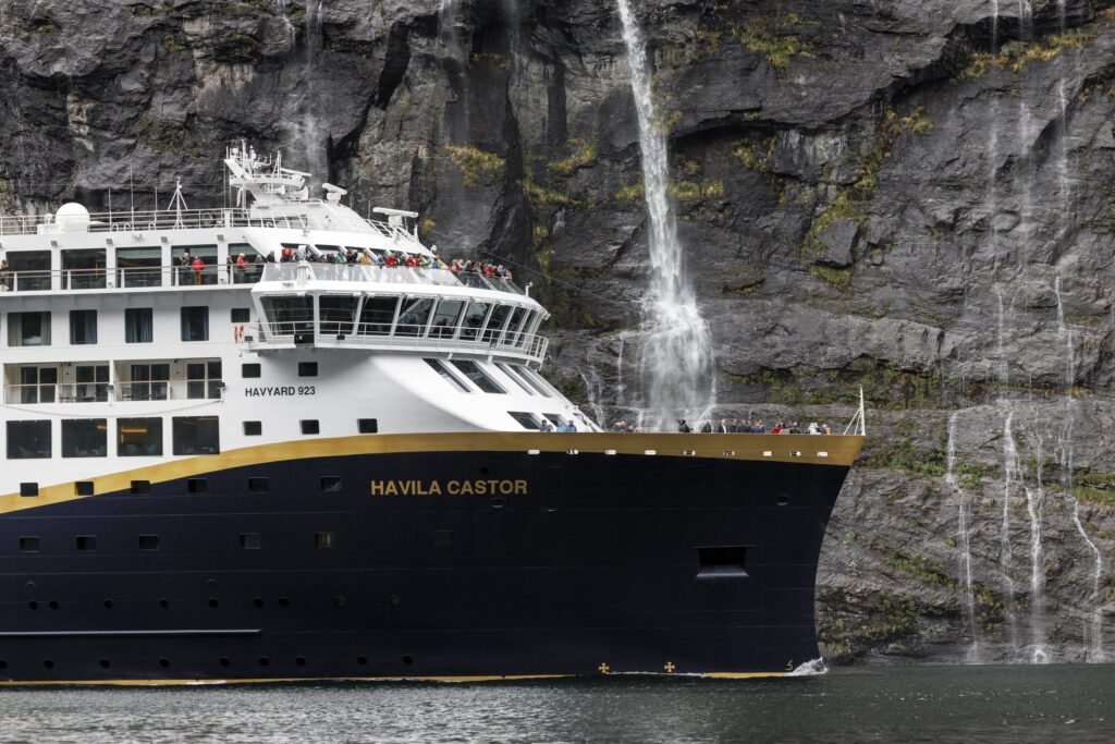 Havila Castor close under a fjord wall, her name on the bow
