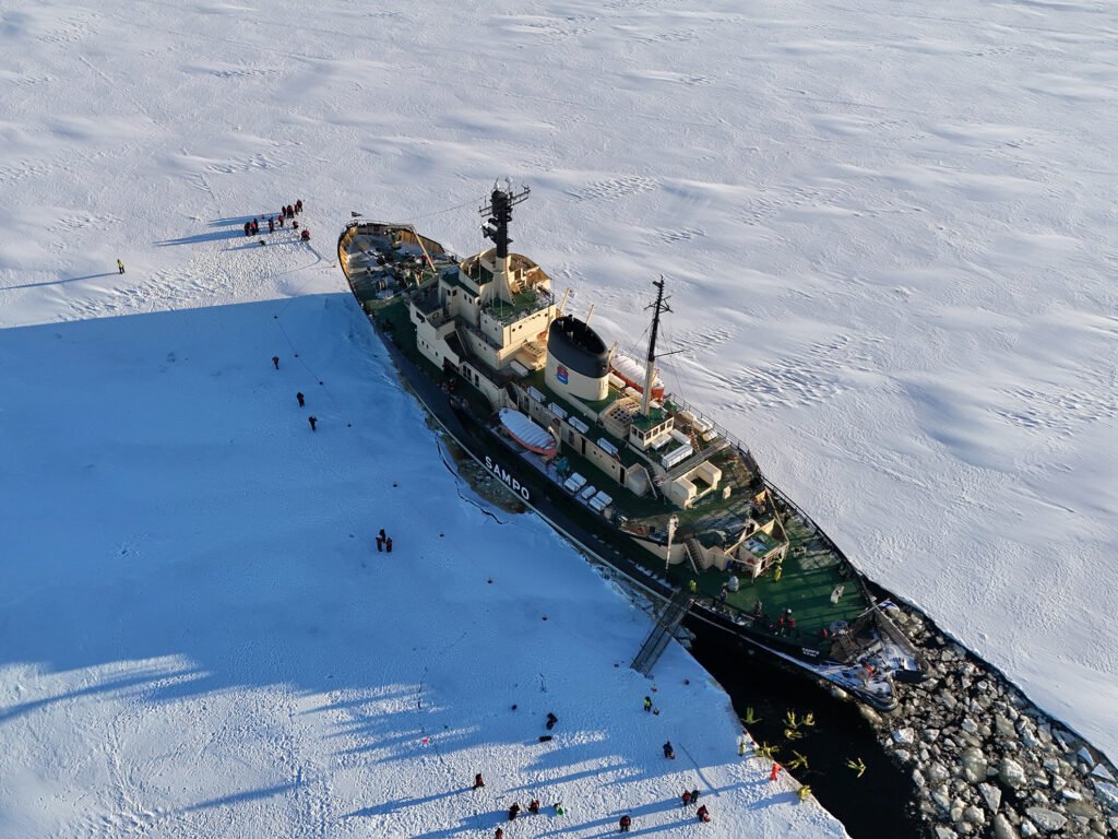 Guests floating in the ice in red survival suits beside the Sampo icebreaker, Kemi — view 2