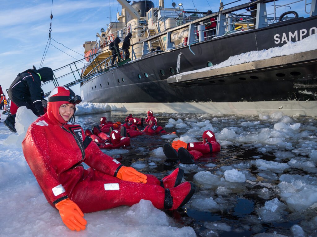 Guests floating in the ice in red survival suits beside the Sampo icebreaker, Kemi