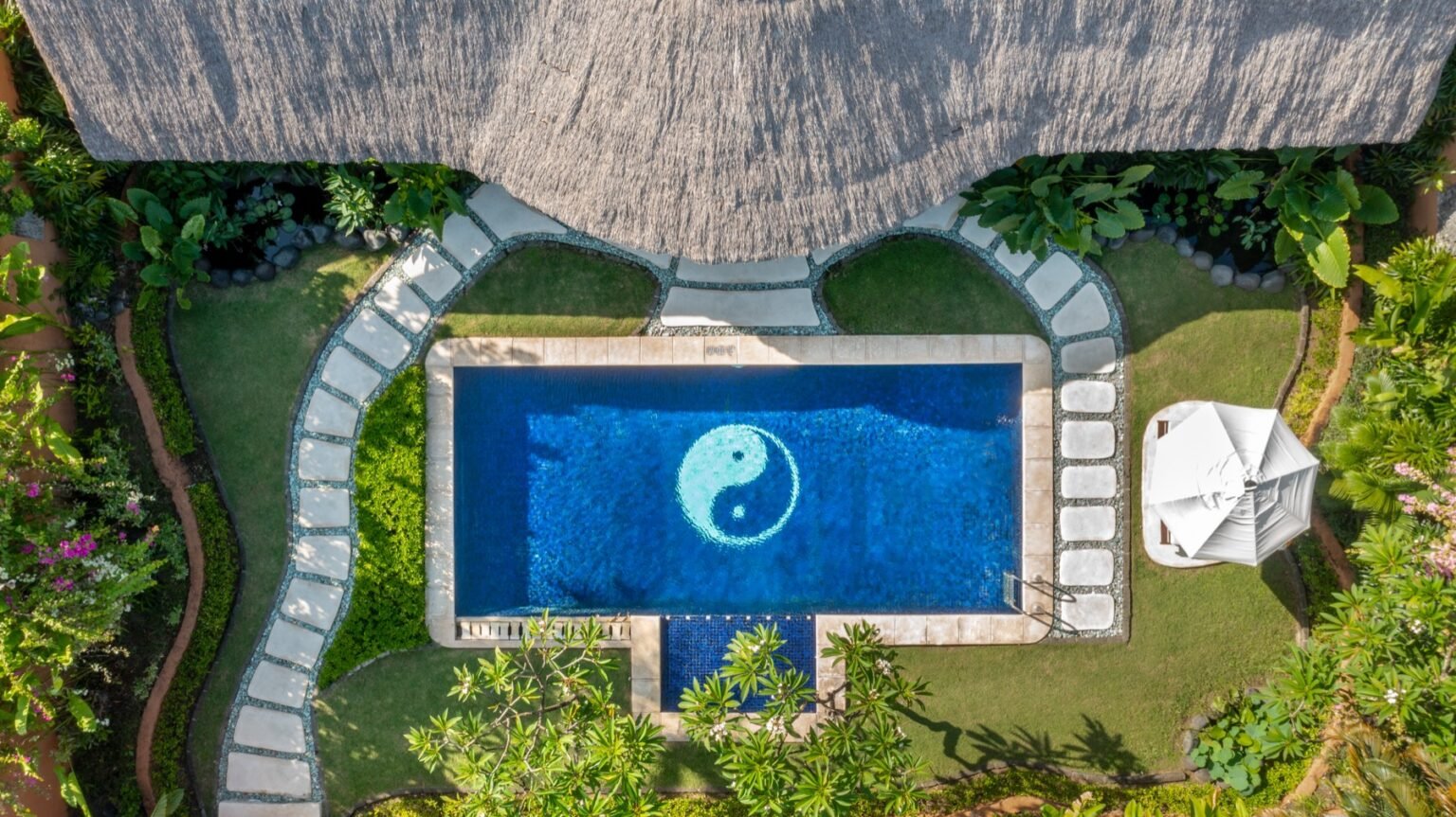 An overhead view of a villa pool with a mosaic pattern on its floor, edged with paving and lawn.