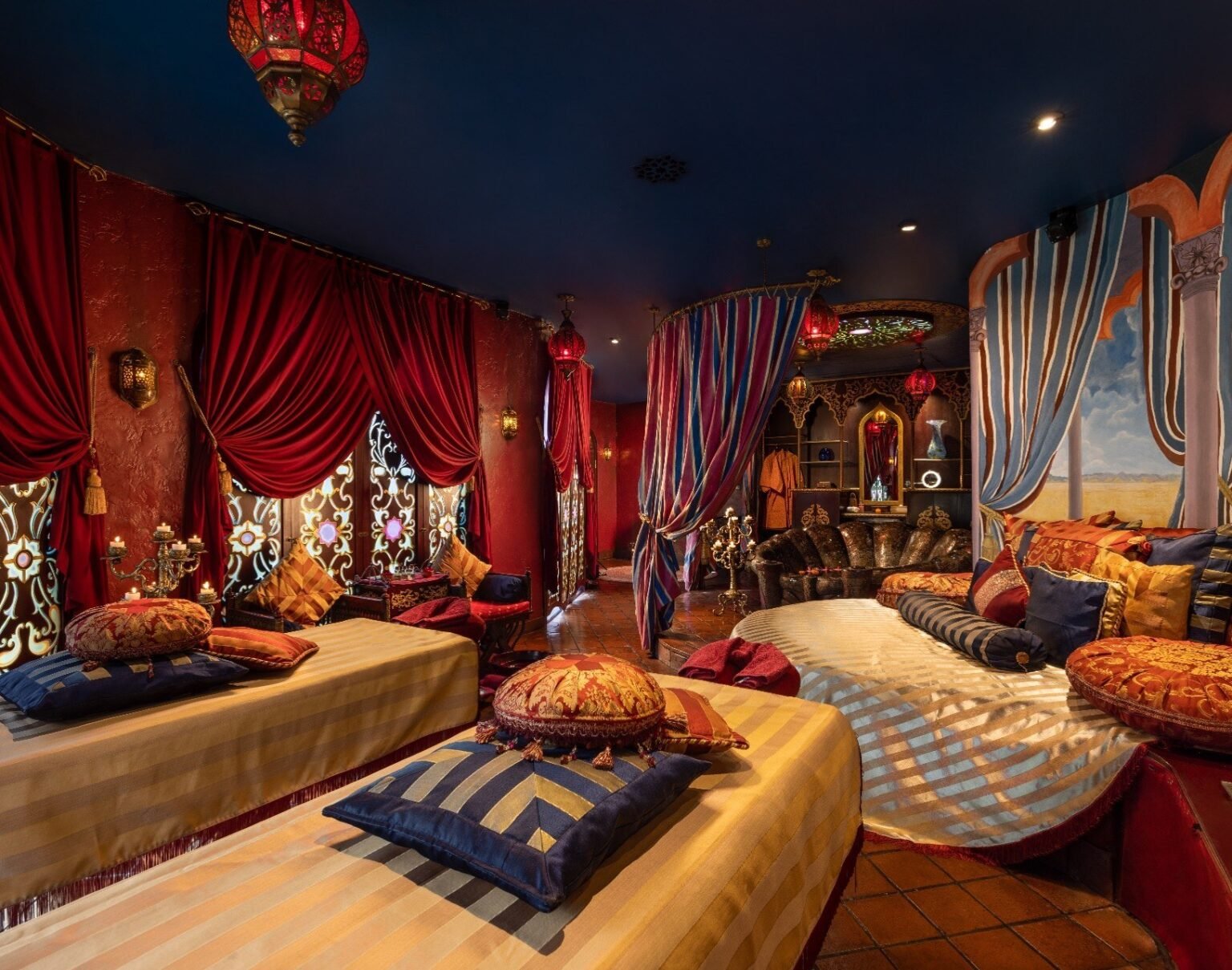 A spa suite with two treatment beds side by side, draped fabric, patterned screens and hanging lanterns.
