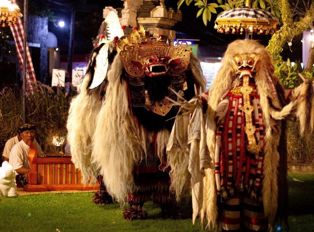 Two large Balinese masked costume figures performed on the lawn at night under a lit parasol.
