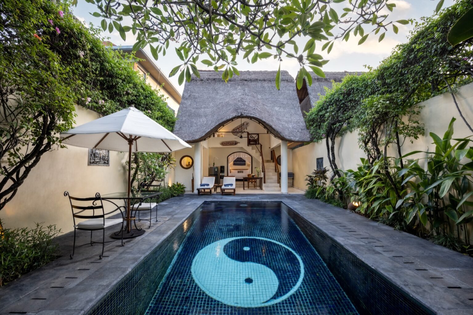 A villa photographed from above with a long rectangular pool beside a paved sun deck.