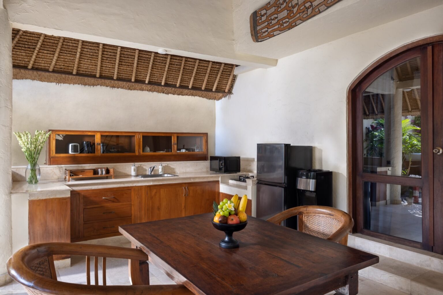 An open-sided villa dining area with a wooden table and chairs under a high thatched roof.