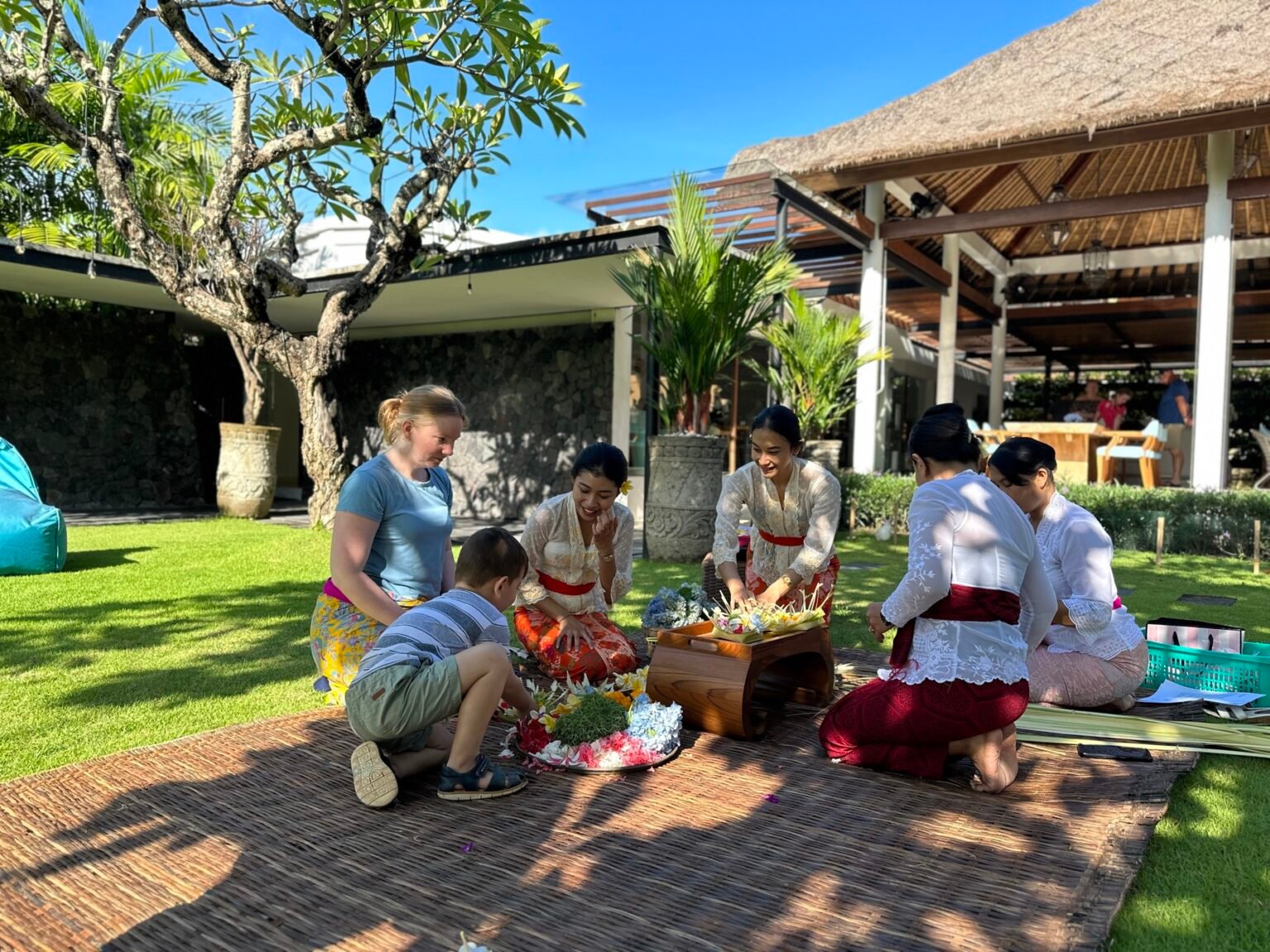 People kneeling on a lawn arranging flowers and palm leaves into Balinese offerings.