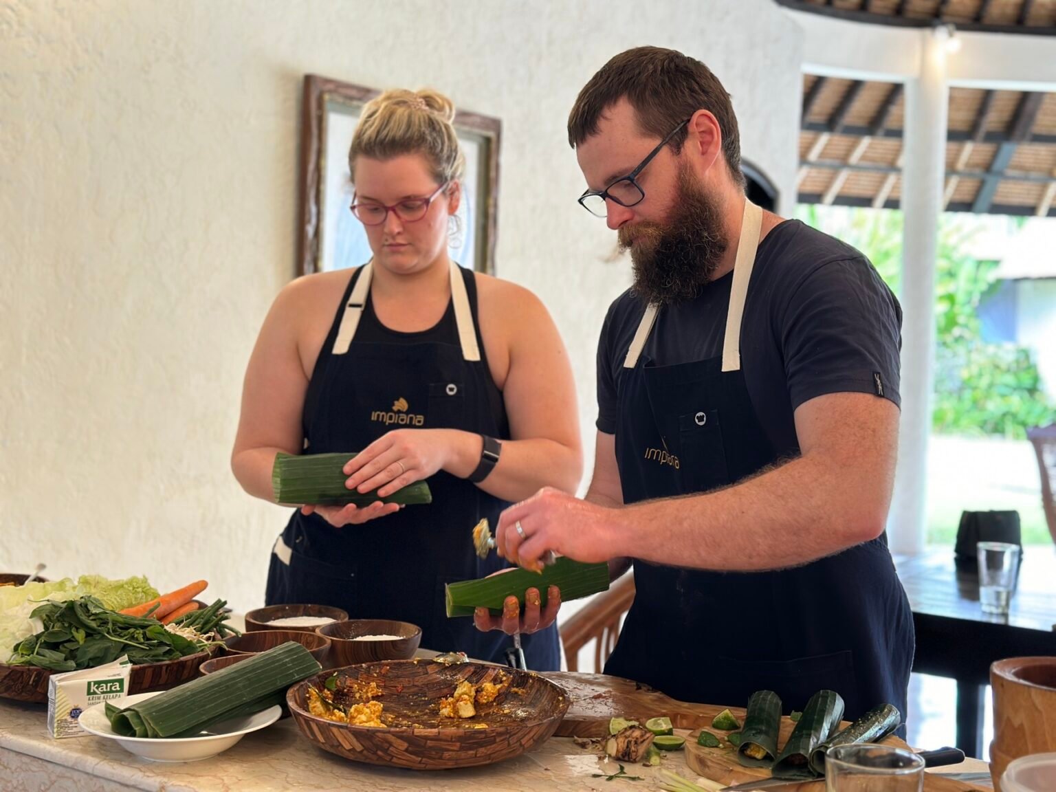 Two people in aprons preparing food at an outdoor kitchen counter.