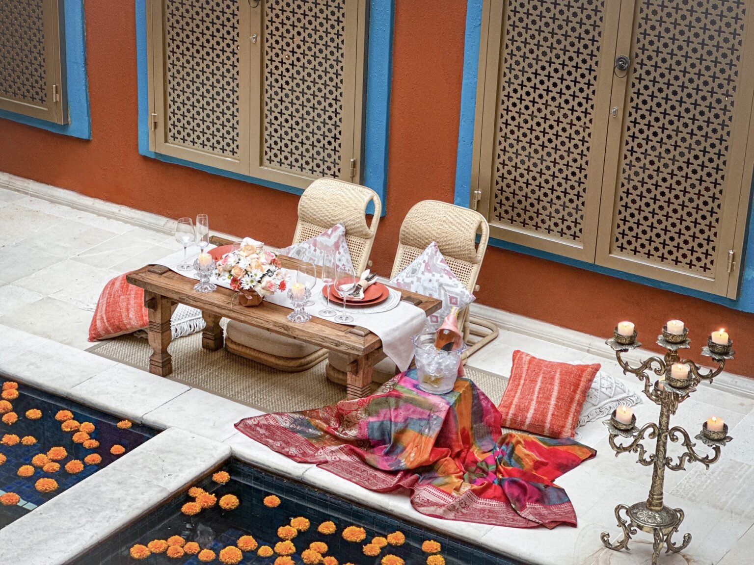 An ornate dinner setting on a terrace with cushions, candelabra and patterned textiles.