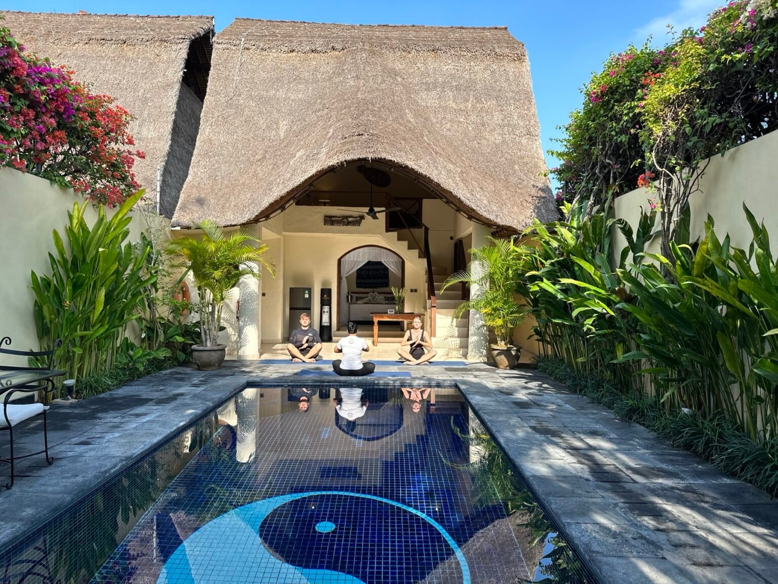 A villa pool with a thatched pavilion at its head, seen down the length of the water.
