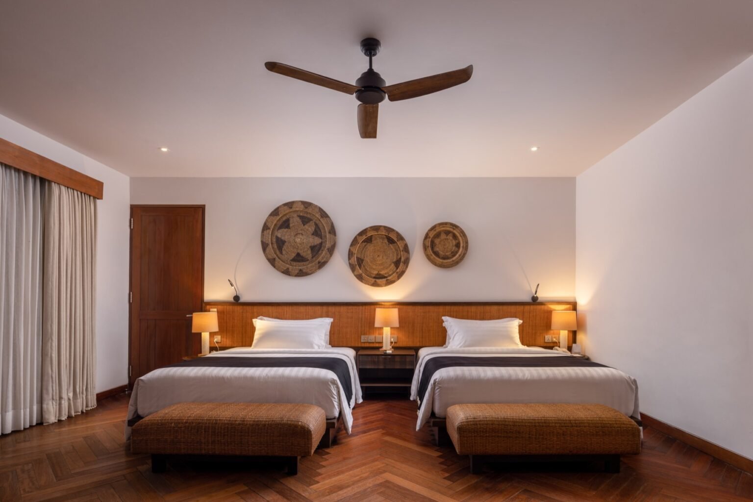 A bedroom with two single beds side by side beneath round woven wall discs.