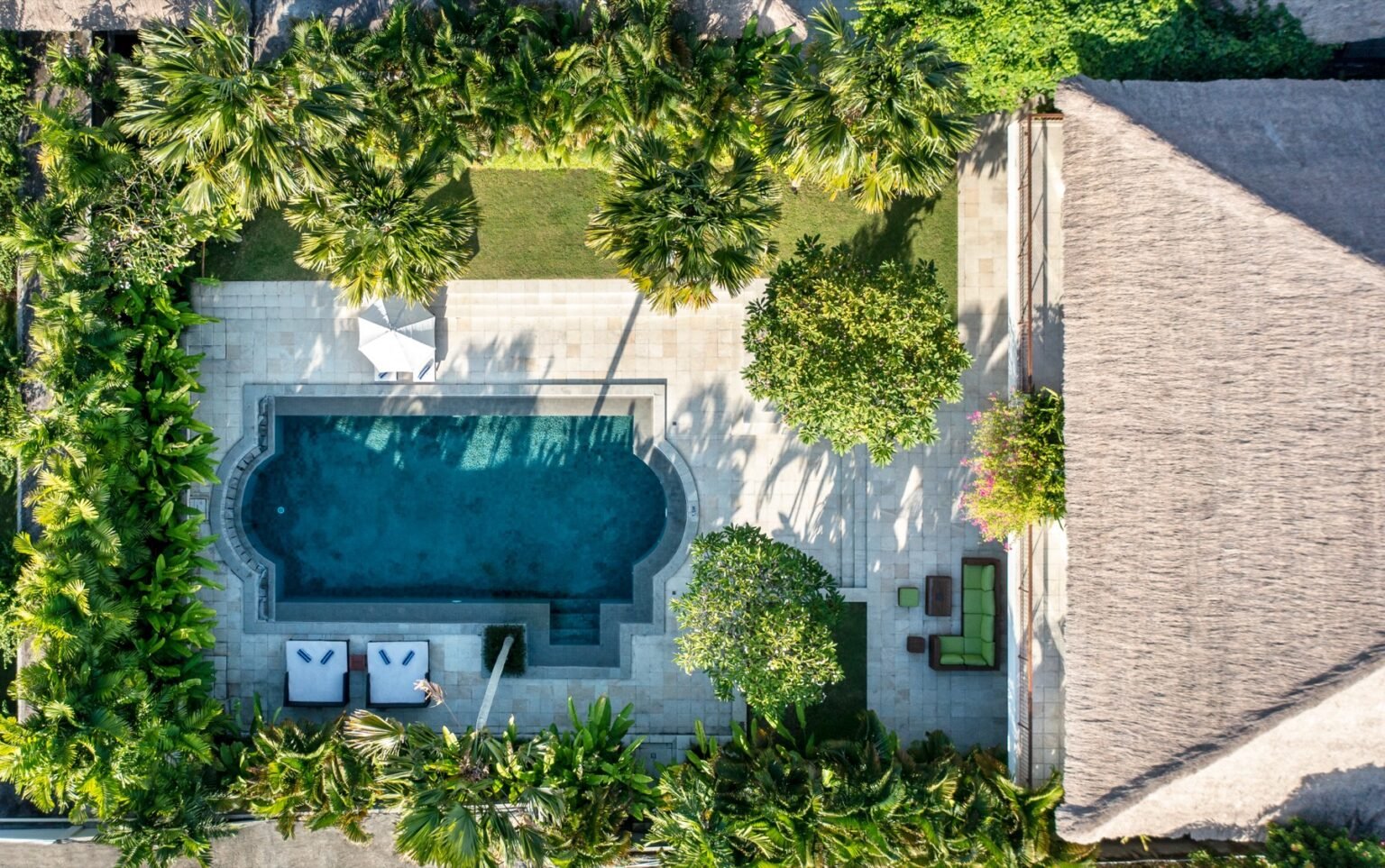 A villa pool with sun loungers on the paving and a two-storey villa behind it.