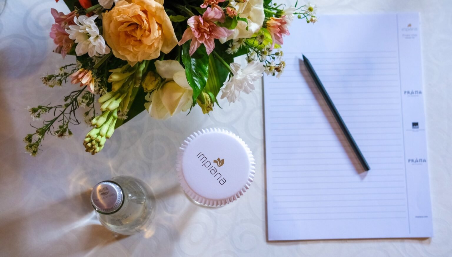 A flower arrangement, a notepad and a pen on a table dressed with white linen.