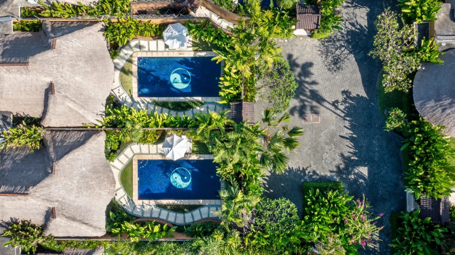 A single villa seen from above, showing the pool, sun deck and thatched roof within its garden walls.