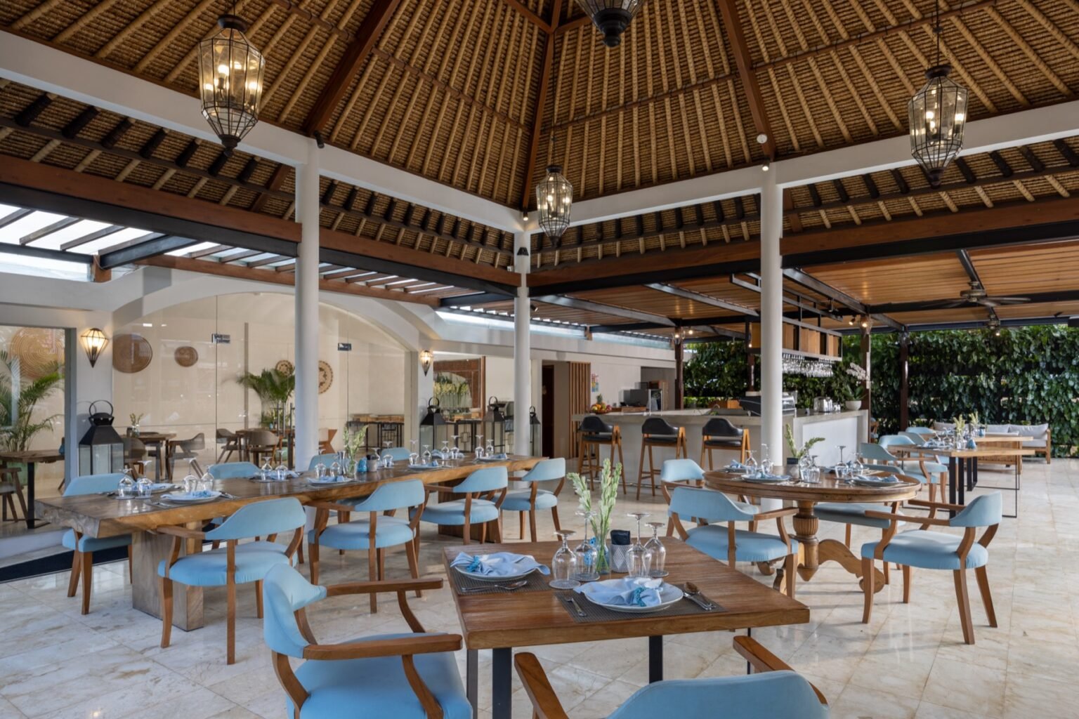 A covered open-air restaurant terrace with tables set for dining and a bar counter behind.