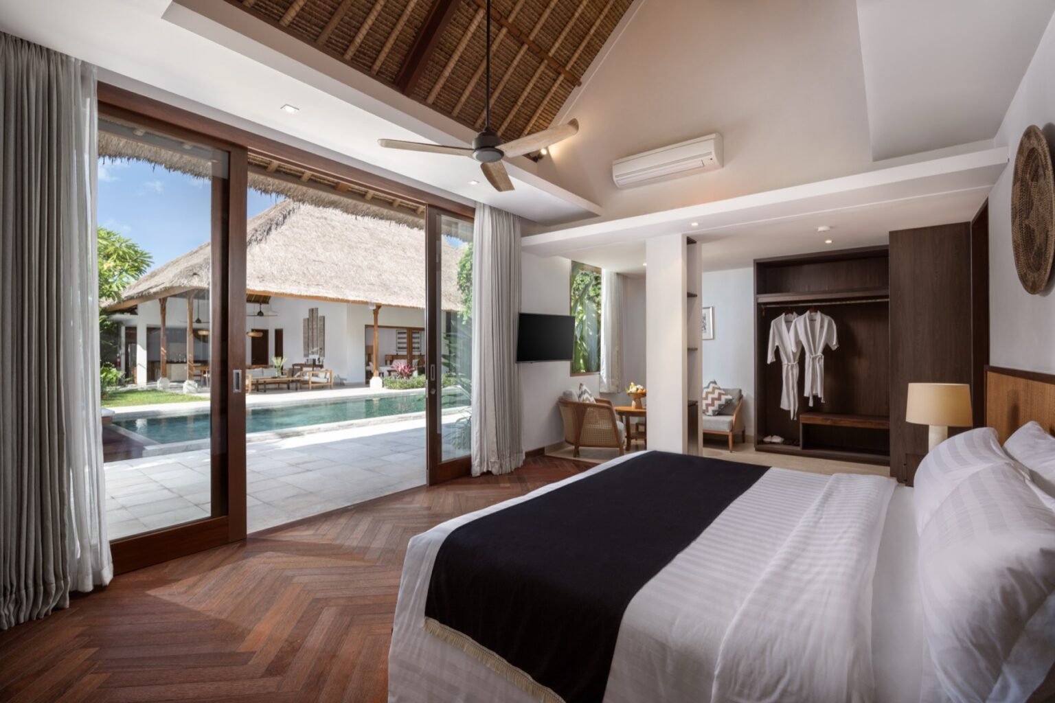 A villa bedroom with a large bed and sliding doors opening onto the pool terrace.