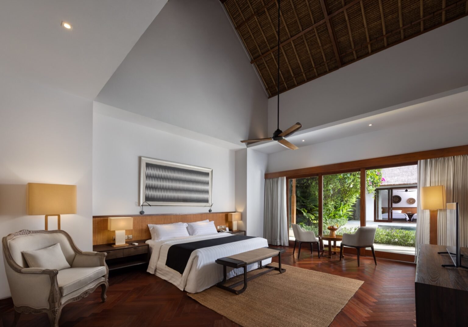 A villa bedroom with a large bed, dark timber furniture and glass doors to the garden.