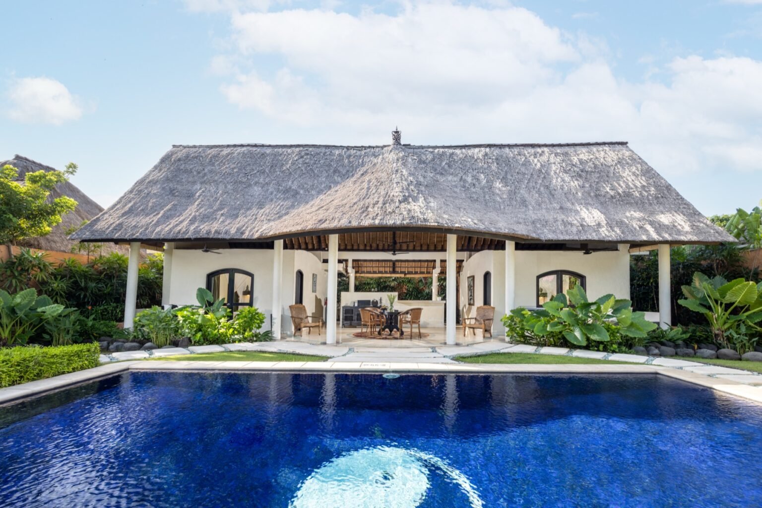 A villa swimming pool edged with stone paving, with garden planting along both sides.