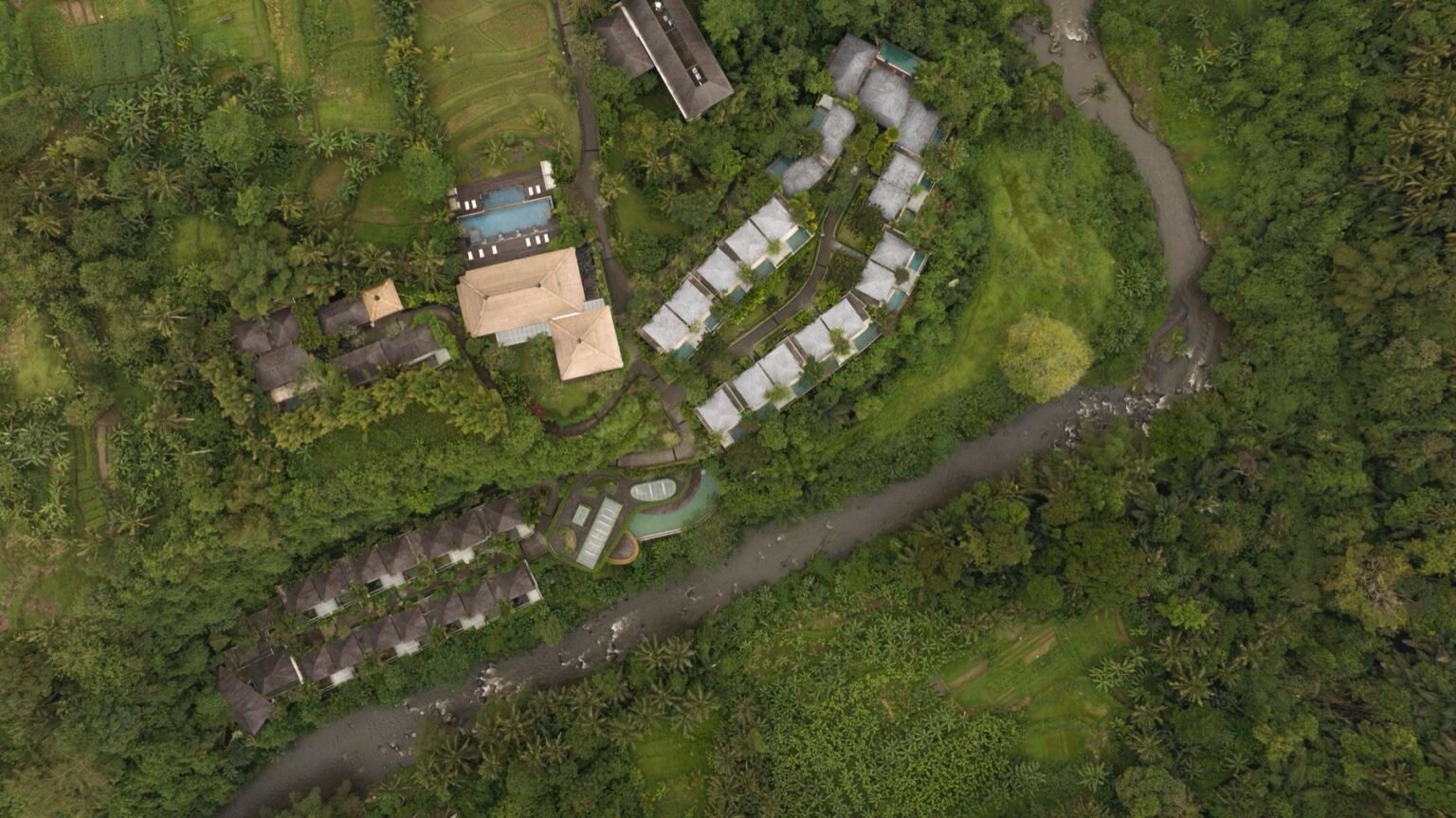 An aerial view of villa roofs and pools set into terraced jungle.