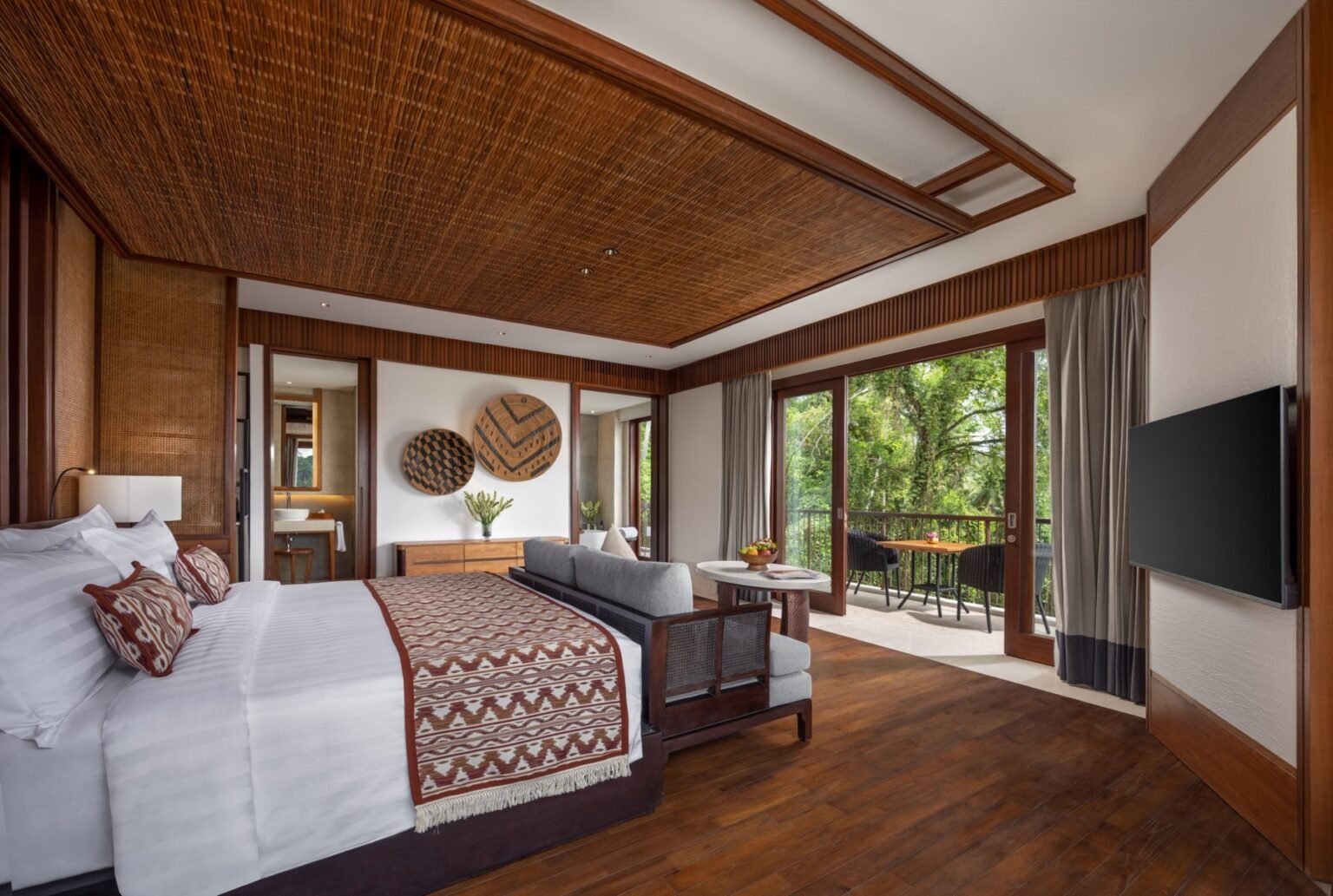 A suite interior with a king bed, timber floor and a seating area by the window.