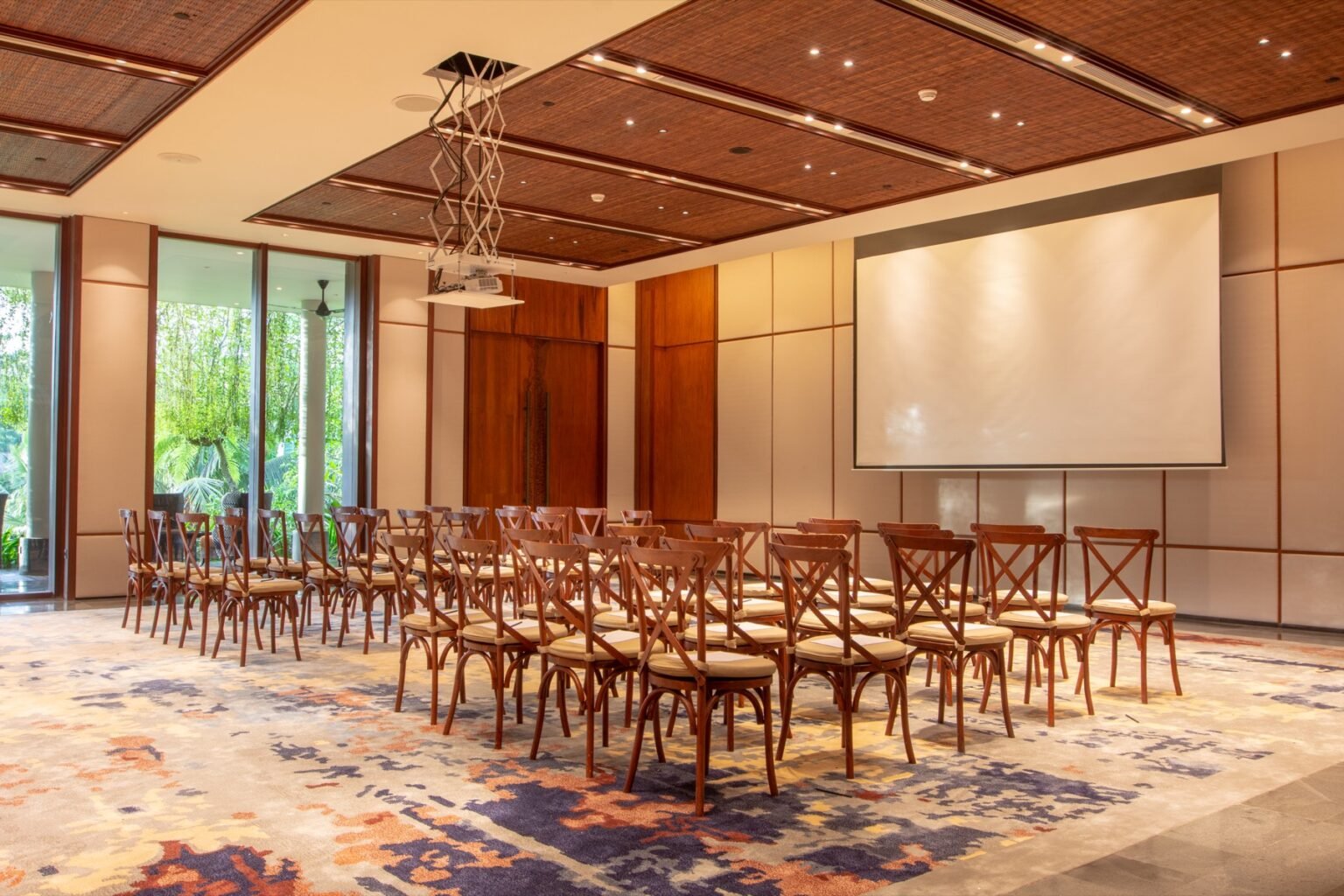 A function room laid out theatre style with rows of wooden chairs facing a projection screen.