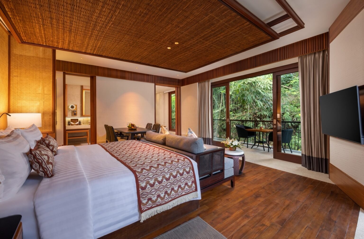 A suite with a king bed, woven wall panels and a balcony beyond.