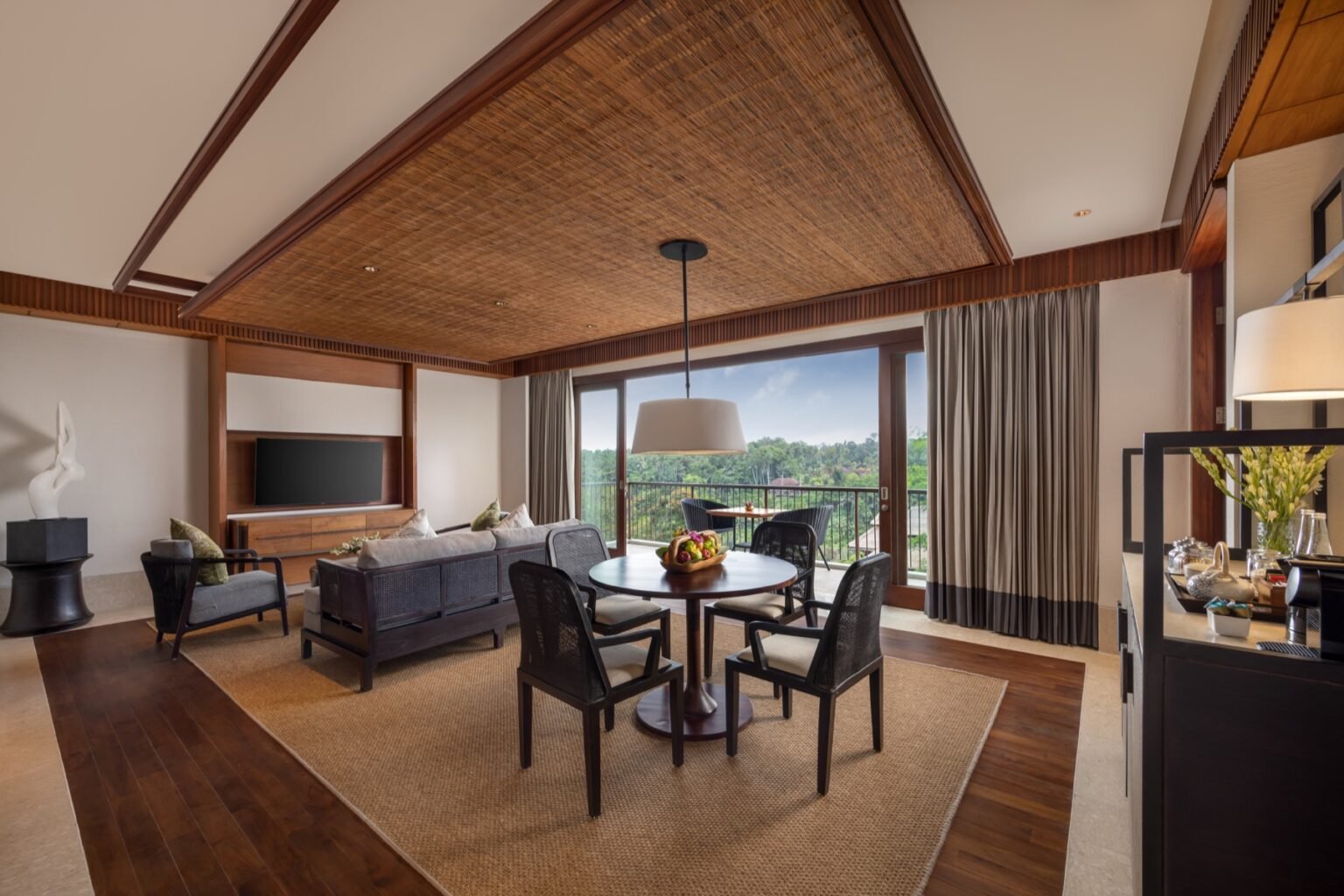 A suite living and dining area with a table and chairs beside full-height windows.