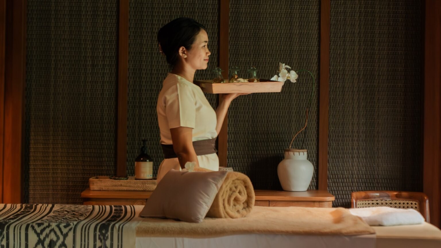 A spa treatment room with two beds and timber screens open to greenery.