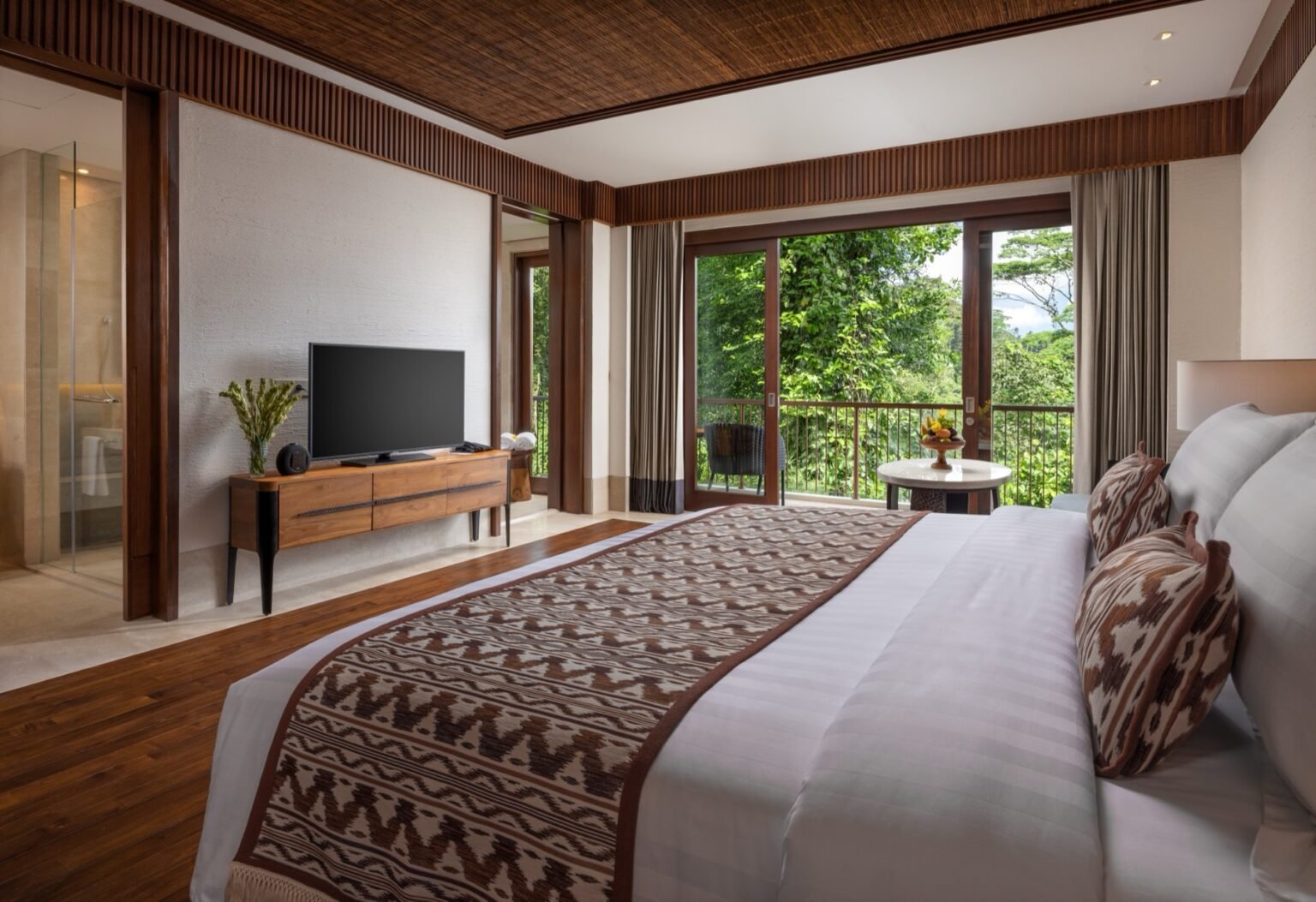 A suite with a large bed under a peaked timber ceiling and doors opening to a balcony.
