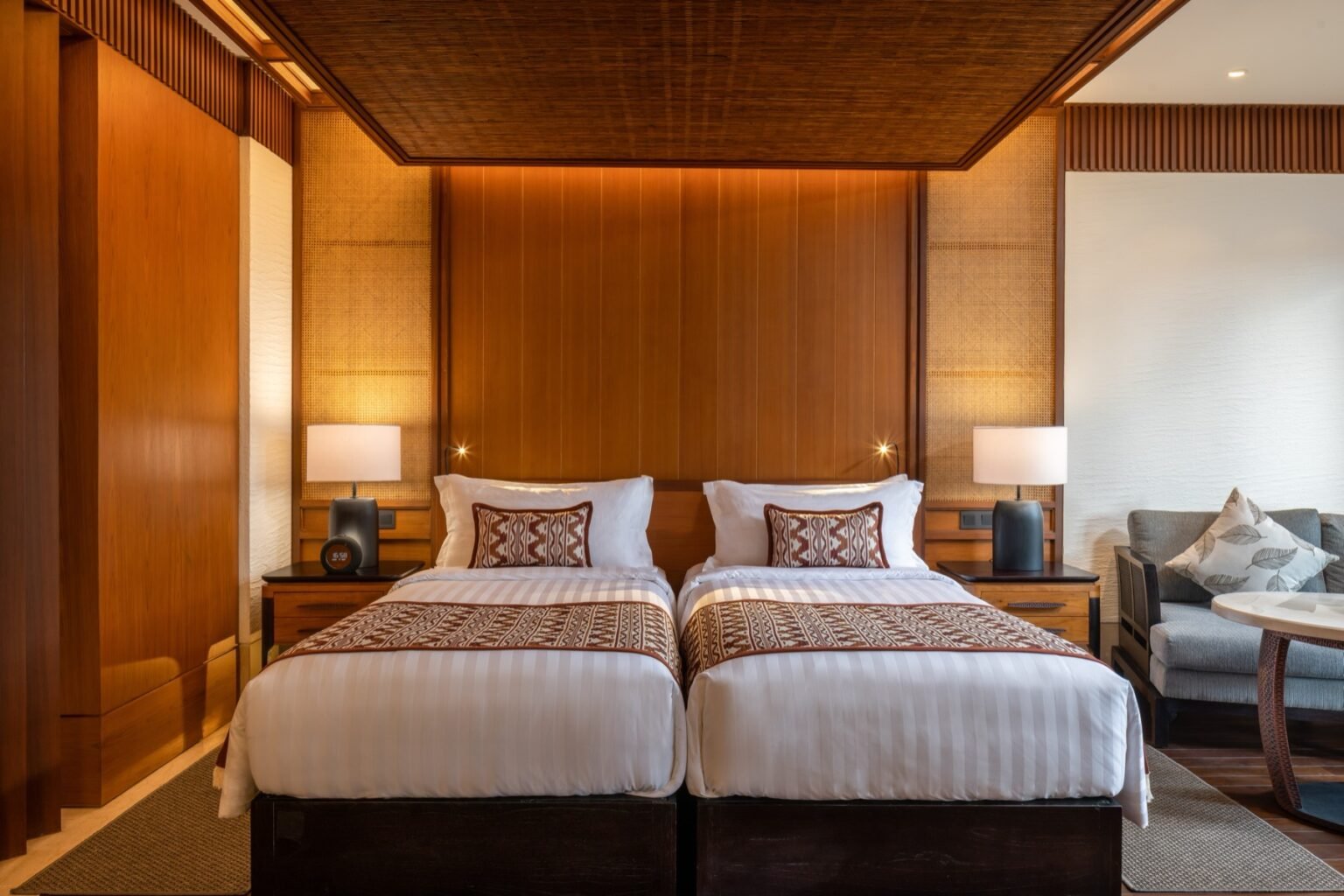 A suite bedroom with two single beds side by side and a seating area beyond.