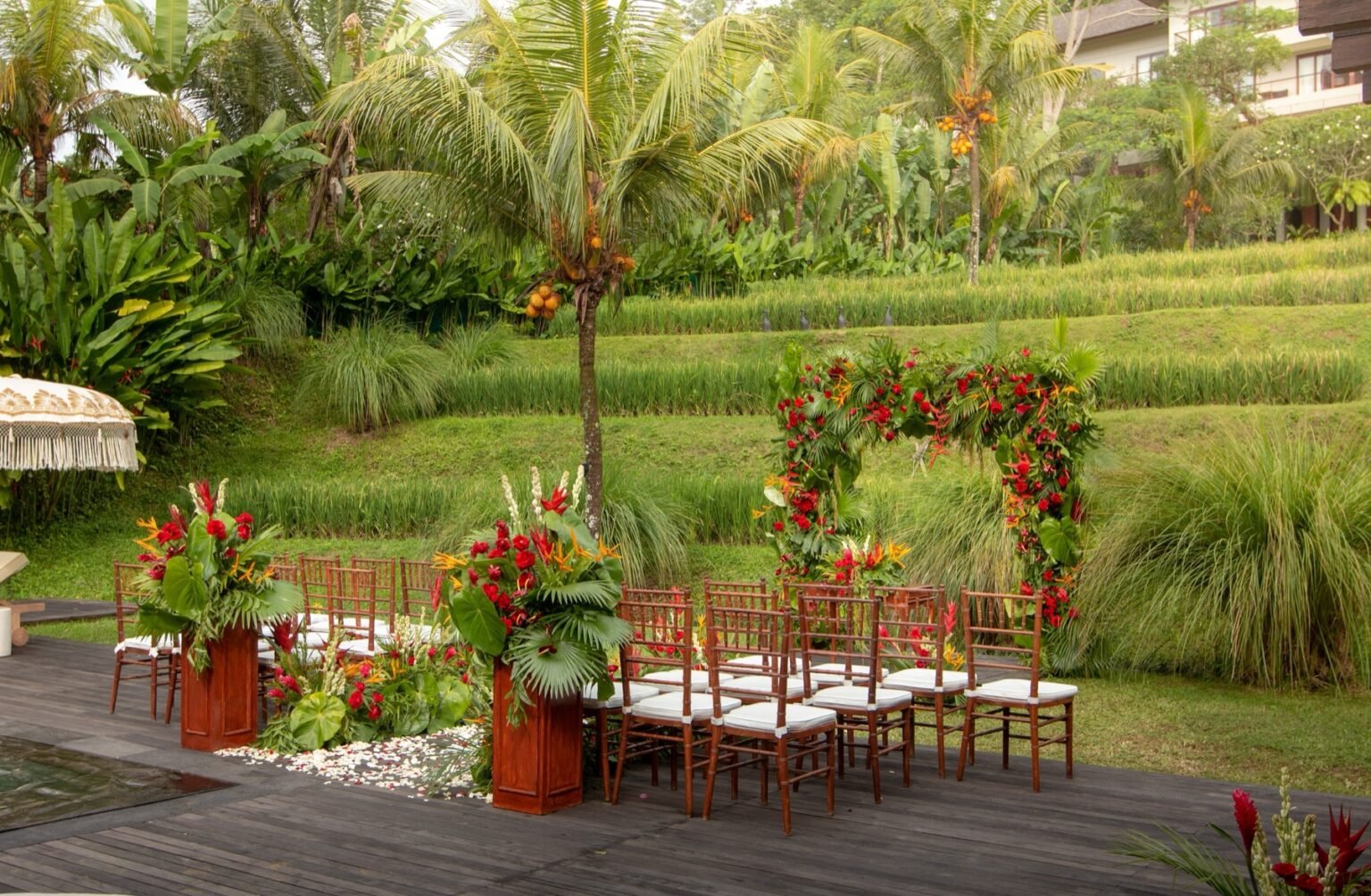 A ceremony arch dressed with red and green foliage on a lawn, with chairs set out in front of it.