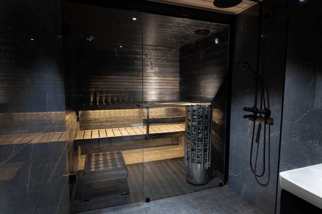 A sauna with timber benches behind glass, beside a shower, inside an apartment