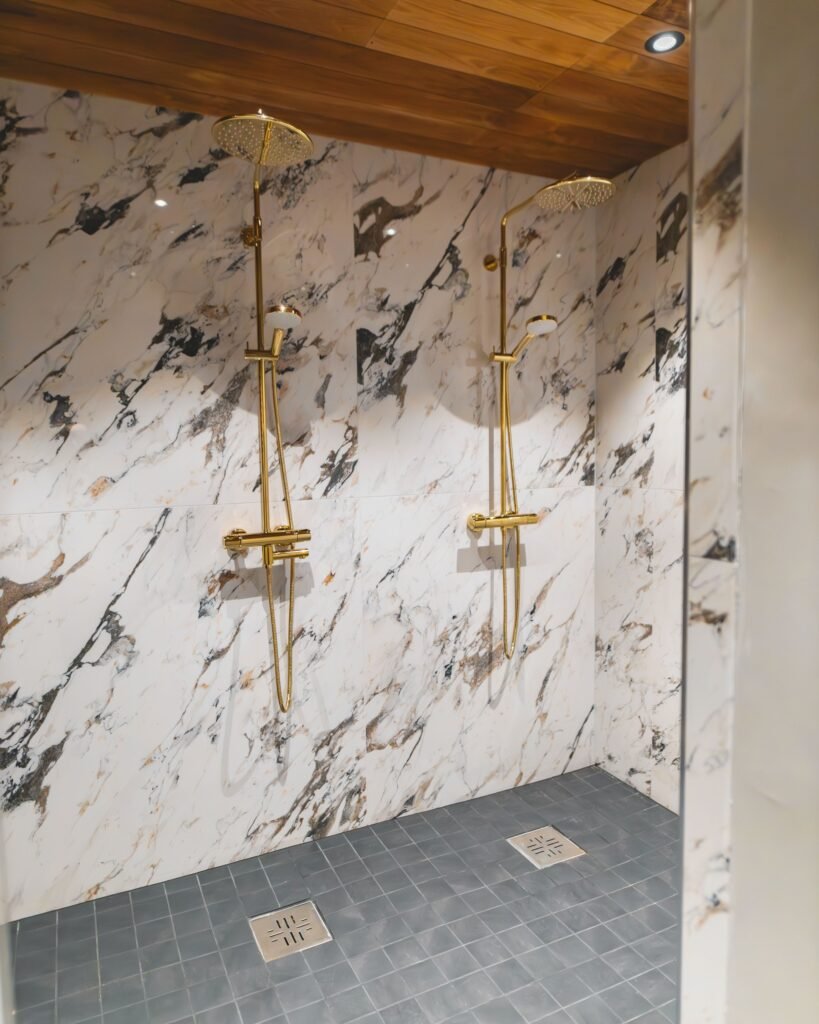 A twin walk-in shower with brass fittings against a marble wall