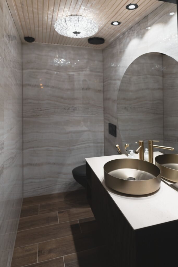 Two brass basins on a stone counter in a bathroom with a walk-in shower